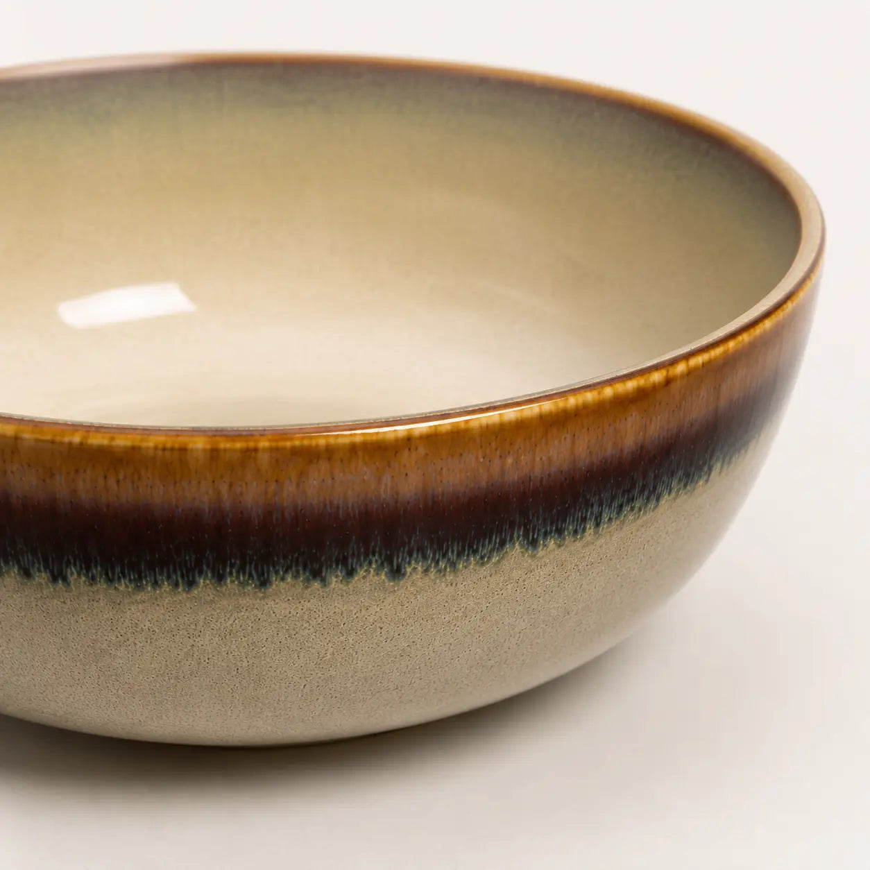 Close-up of beige ceramic matcha bowl with brown rim and dark drip glaze detail