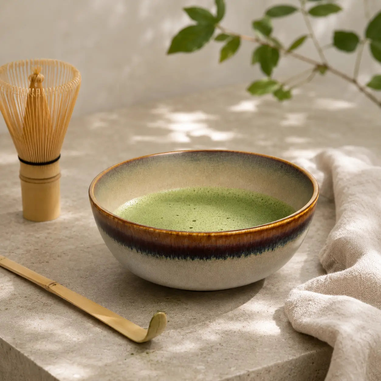 Beige ceramic matcha bowl styled with bamboo whisk, matcha tea, and tea spoon