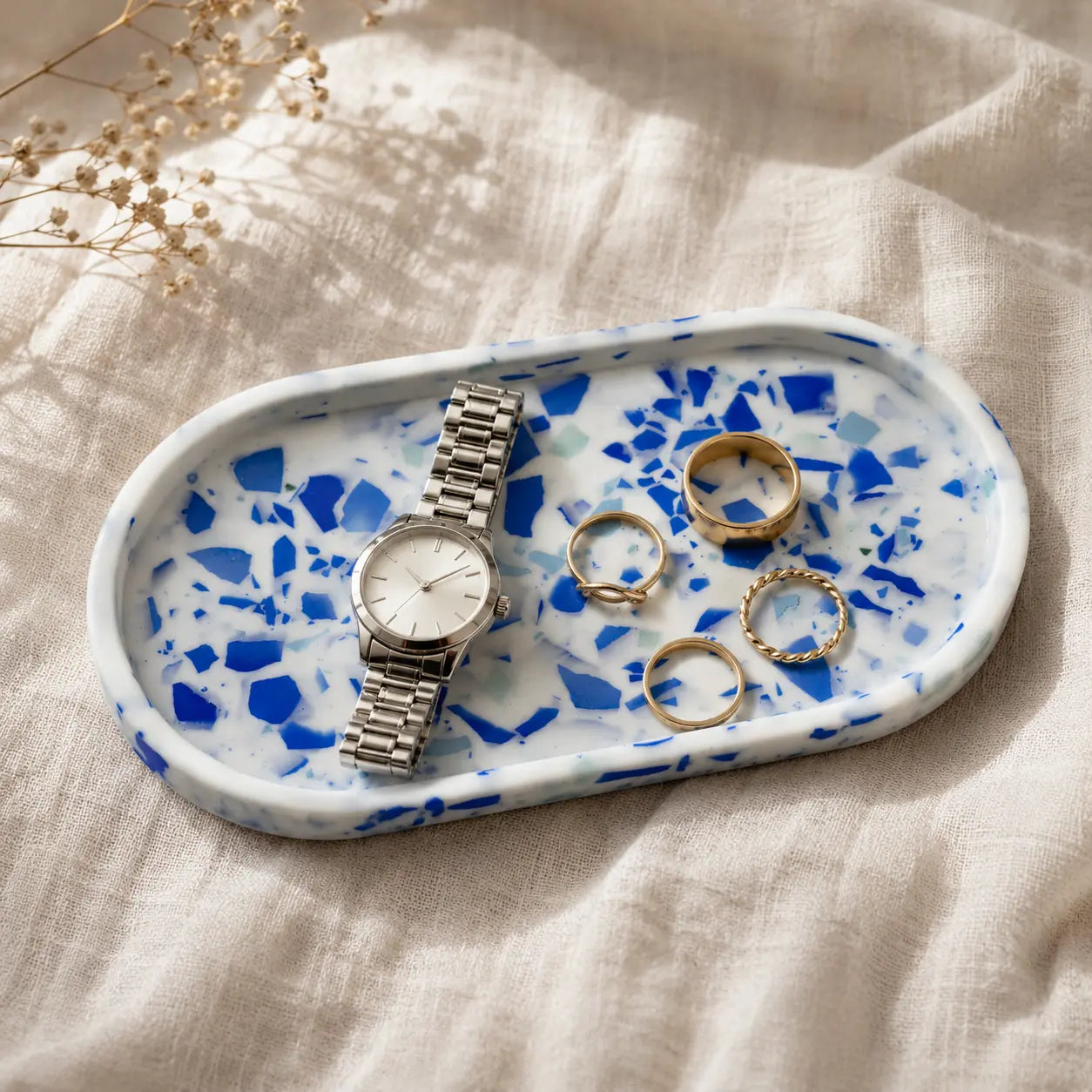 Blue terrazzo jewelry tray with watch and gold rings on linen fabric